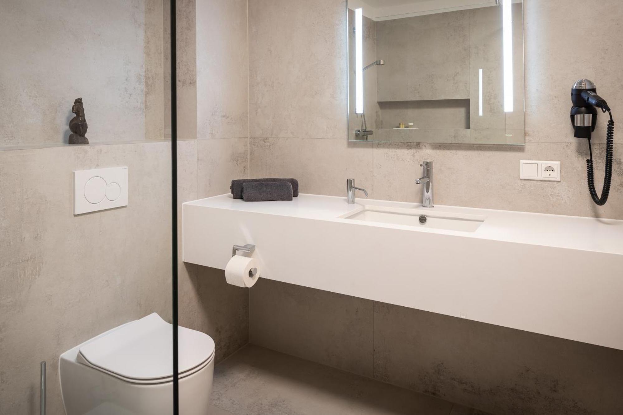 A modern bathroom with a white sink, a mirror, a hairdryer, and a toilet.
