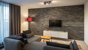 Un salon moderne avec un canapé gris, une table basse et un téléviseur à écran plat fixé à un mur texturé.