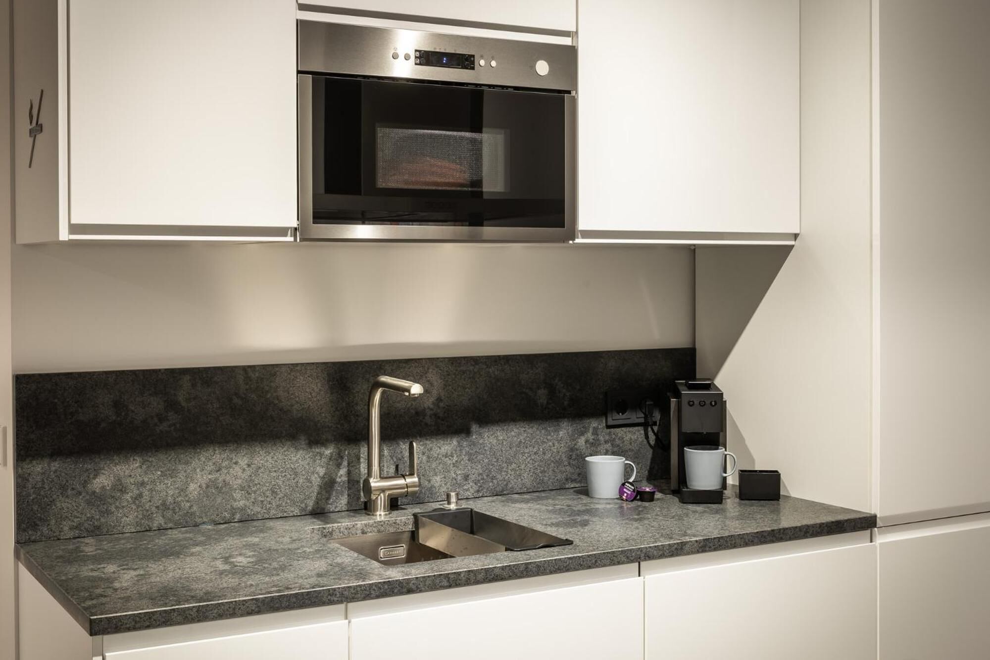 A modern kitchen with a built-in oven, a stainless steel sink, and a coffee maker.
