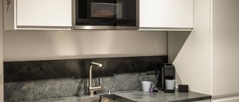 A modern kitchen with a built-in oven, a stainless steel sink, and a coffee maker.