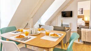 Un comedor con mesa de madera, sillas y productos para el desayuno, como croissants y zumo de naranja.