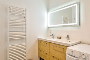 Un baño con lavamanos blanco, espejo y toallero.