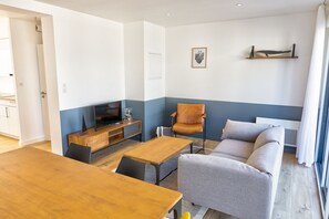 Una sala de estar moderna con una mesa de comedor de madera, un sofá y un televisor sobre un mueble de madera.