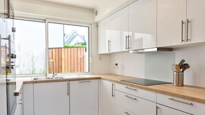 A modern kitchen with white cabinets, a wooden countertop, and a window overlooking a garden. - Les Docks (Combrit)