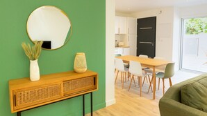 A modern living space with a green accent wall, a round mirror, a console table with decorative items, a dining area with a wooden table and chairs, and a black door leading to a kitchen. - L'Eden - Duplex with Tertace (Combrit)