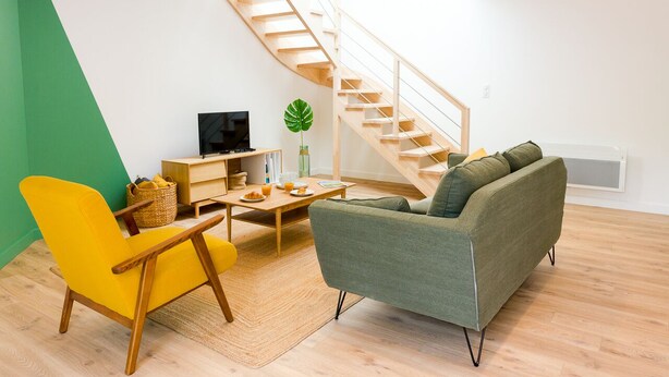 A modern living room with a wooden staircase, a yellow armchair, a green sofa, and a wooden coffee table. - L'Eden - Duplex with Tertace (Combrit)