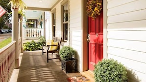 A porch with a red door, a bench, and potted plants.