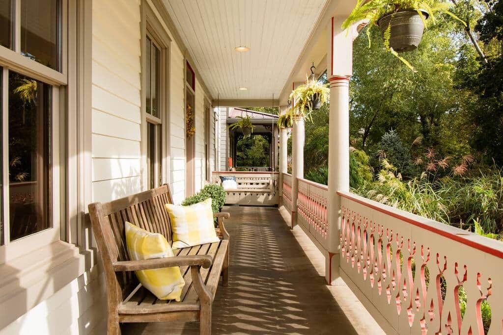 A covered porch with a wooden bench, potted plants, and a decorative railing.