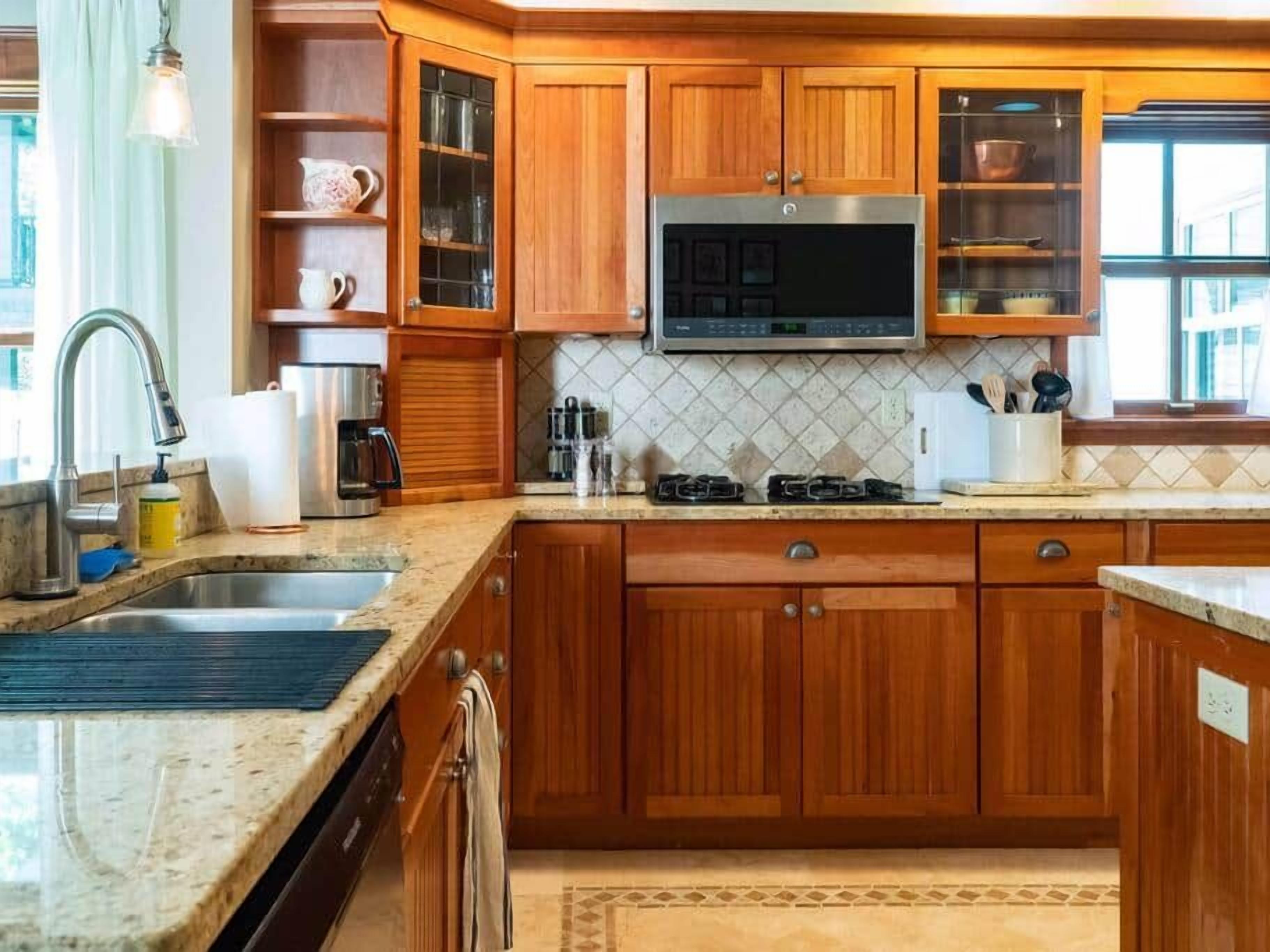 Una cocina con armarios de madera, un microondas de acero inoxidable, una estufa a gas y un fregadero.