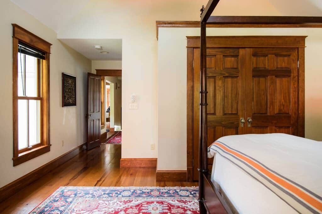 A bedroom with a large bed, wooden flooring, a patterned rug, and a wooden wardrobe.