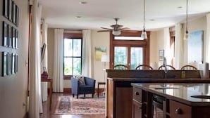 A kitchen with a central island, wooden cabinets, a ceiling fan, and a dining area with a chair and rug.