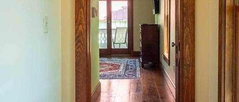 A hallway with wooden flooring, a door on the right, and a window at the end.