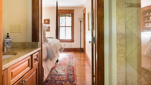 Een smalle gang die leidt naar een slaapkamer met een bed, een raam en een badkamer met een douchecabine.
