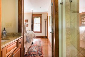 Ein schmaler Flur führt zu einem Schlafzimmer mit Bett, Fenster und einem Badezimmer mit Duschkabine.