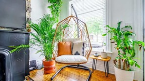 Ein gemütliches Wohnzimmer mit Hängesessel, Kamin und vielen topfpflanzen.
