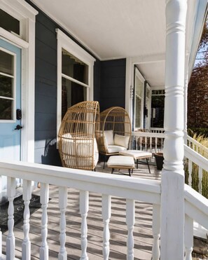 A porch with a white railing, two wicker chairs, and a small table.