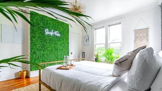 Ein Schlafzimmer mit grüner Wand, einem Bett mit weißer Bettwäsche und einem Nachttisch mit einem Glasbehälter.