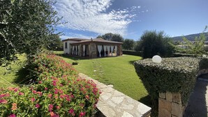 Un bâtiment en pierre, surmonté d’un toit en tuiles, entouré d’une pelouse bien entretenue et de plantes en fleurs.
