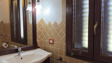A bathroom with a white sink, dark wooden cabinets, a mirror, and a window with frosted glass.