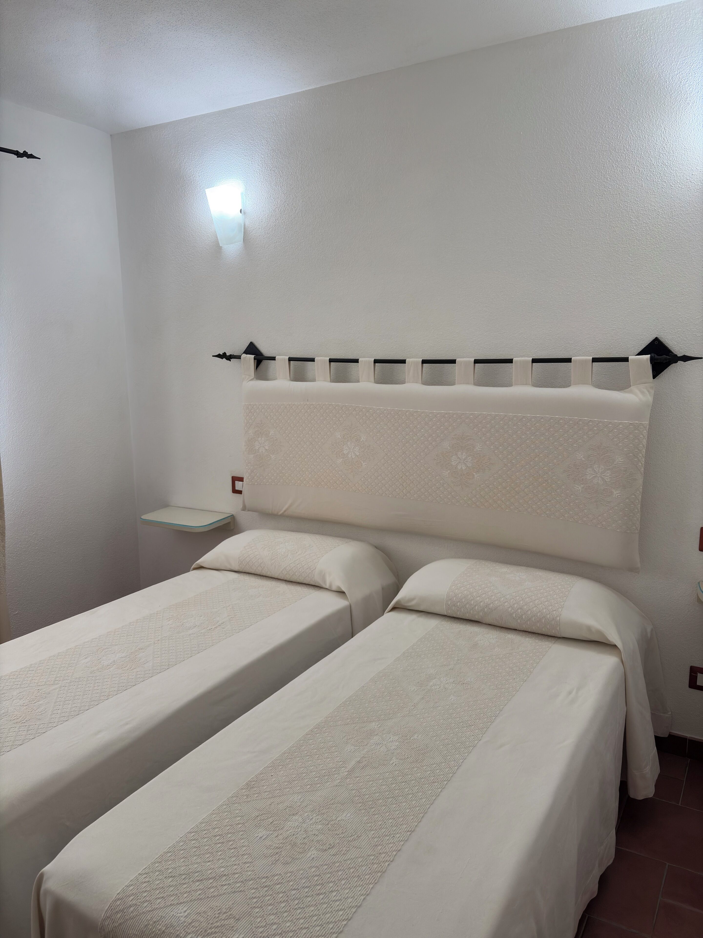 Una habitación con dos camas individuales, una mesita de noche y una lámpara fijada a la pared.