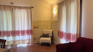 Une pièce avec un mur en pierre, un lit recouvert d’une couverture blanche, un canapé rouge et une table recouverte d’une nappe blanche.