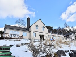 A two-story building with a large chimney, multiple windows, and a snow-covered ground.