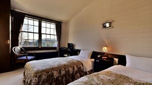 A hotel room with two beds, a desk, a chair, a lamp, and a window with curtains. - Petit Hotel Kanan (Chino)