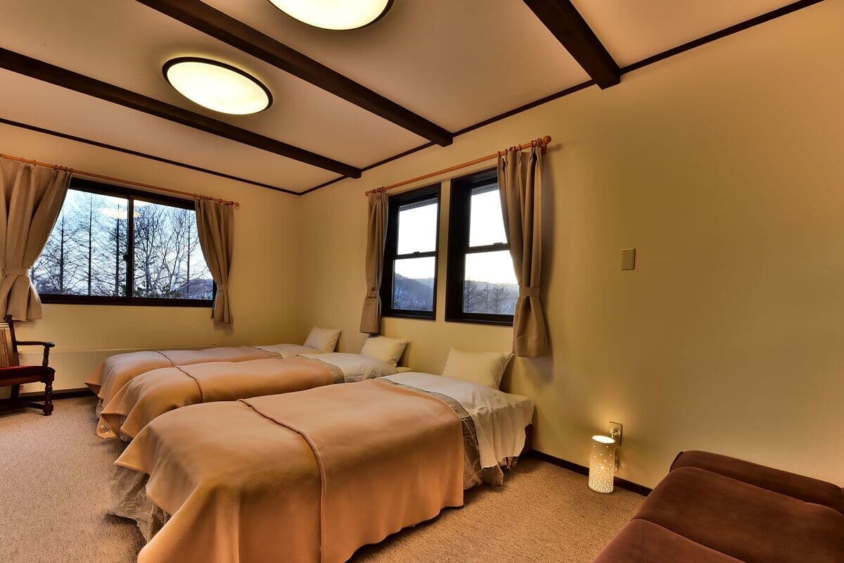 Ein Zimmer mit drei Betten, einem Holzstuhl und einem kleinen Tisch.