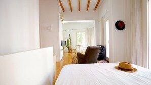 Habitación de hotel con cama, una silla, una maleta, un sombrero y una planta en maceta.