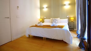 Habitación de hotel con una cama grande, vigas de madera en el techo, dos lámparas de noche y un ventanal con cortinas.
