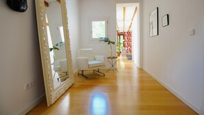Una habitación amplia con un espejo grande, una silla blanca, una mesita pequeña y una planta en maceta.