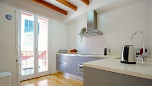 Una cocina moderna con encimera blanca, electrodomésticos de acero inoxidable y un puerta corrediza de vidrio que da a un balcón.