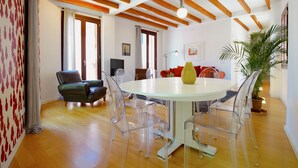 Una sala de estar moderna con una mesa redonda de cristal, sillas transparentes, un sofá verde y vigas de madera en el techo.