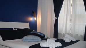 A neatly made bed with white linens, a dark blue headboard, and a blue pillow. There are two white towels folded on the bed. - Molo 5 (Naples)