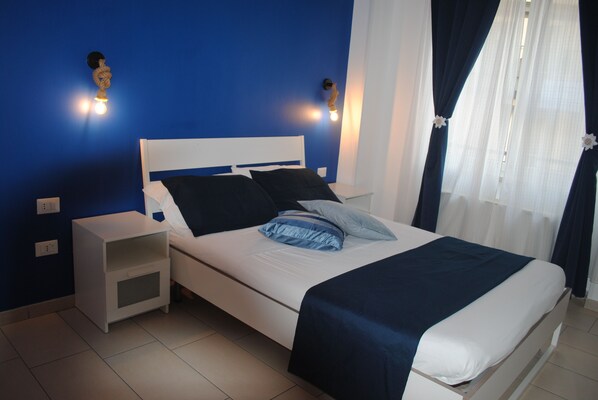 A neatly made bed with a white headboard and blue bedding, a small bedside table, and a wall-mounted light fixture.