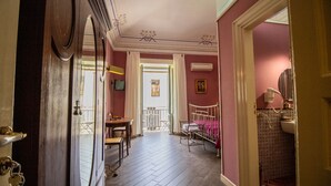 A hallway with a wooden floor, a dining area with a table and chairs, a bed with a metal frame, and a bathroom with a sink and mirror. - THE PALACE B&B and Apartments - FLOWER LUXURY ROOM (Santo Stefano di Camastra)