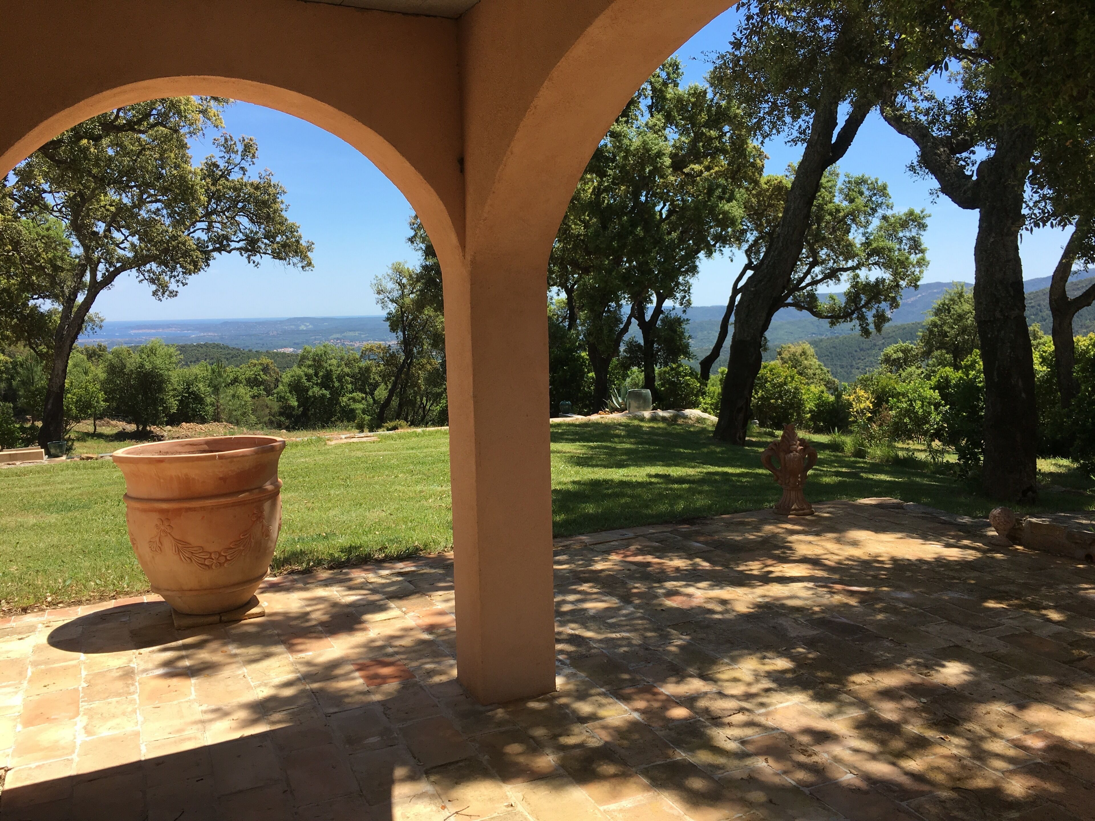 A covered patio area with a large terracotta pot, a fire hydrant, and a view of a vineyard and distant hills.