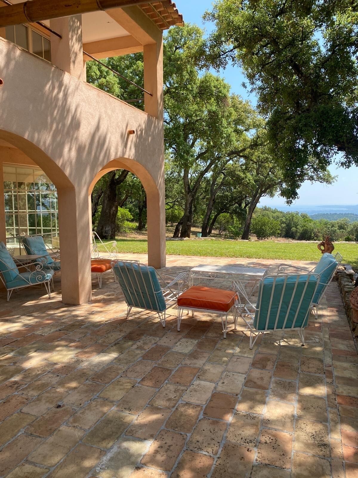 Un patio couvert avec des meubles d’extérieur, une vue sur les arbres et un paysage lointain.