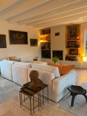 A living room with a sectional sofa, a small table with a bust sculpture, a black stool, and a fireplace.