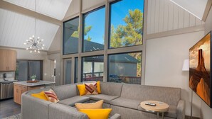 Ein modernes Interieur mit einer Eckcouch, einem kleinen runden Tisch und einem großen Fenster mit Blick auf Bäume.