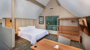Ein Hotelzimmer mit Bett, Schreibtisch, Stuhl, Deckenventilator, Fenster und einem Bild an der Wand.