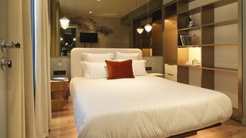 A modern hotel room with a large bed, bedside tables, a TV, and a built-in bookshelf.