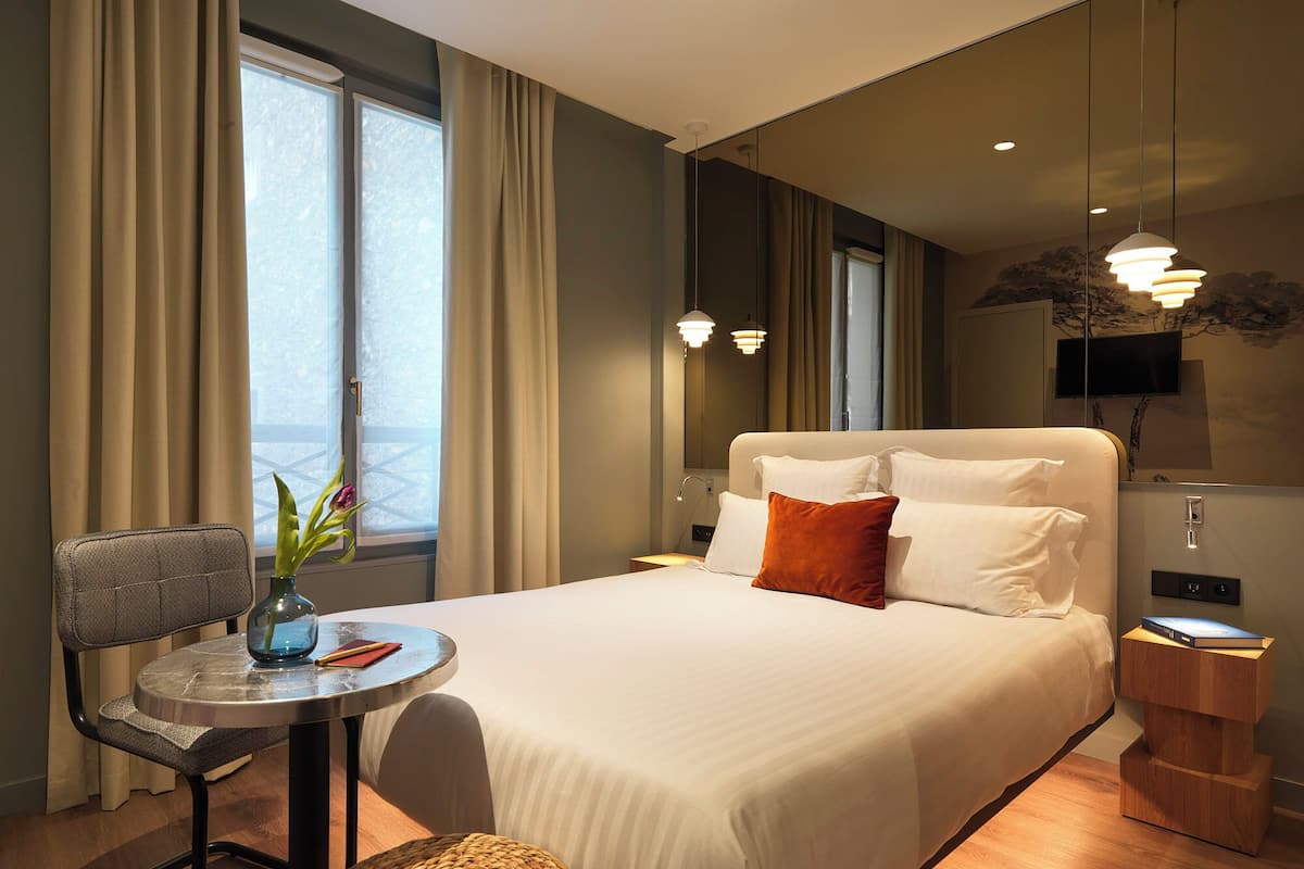Ein Hotelzimmer mit einem Bett, einem kleinen Tisch mit Stuhl, einem Fernseher und einem Fenster mit Vorhängen.