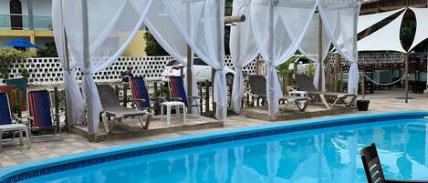 A swimming pool with lounge chairs and a covered seating area.