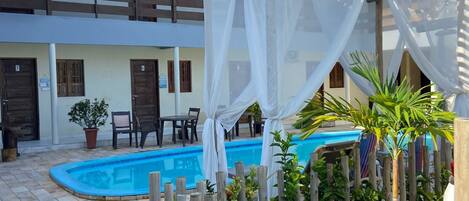 A courtyard with a swimming pool, wooden fence, and potted plants.
