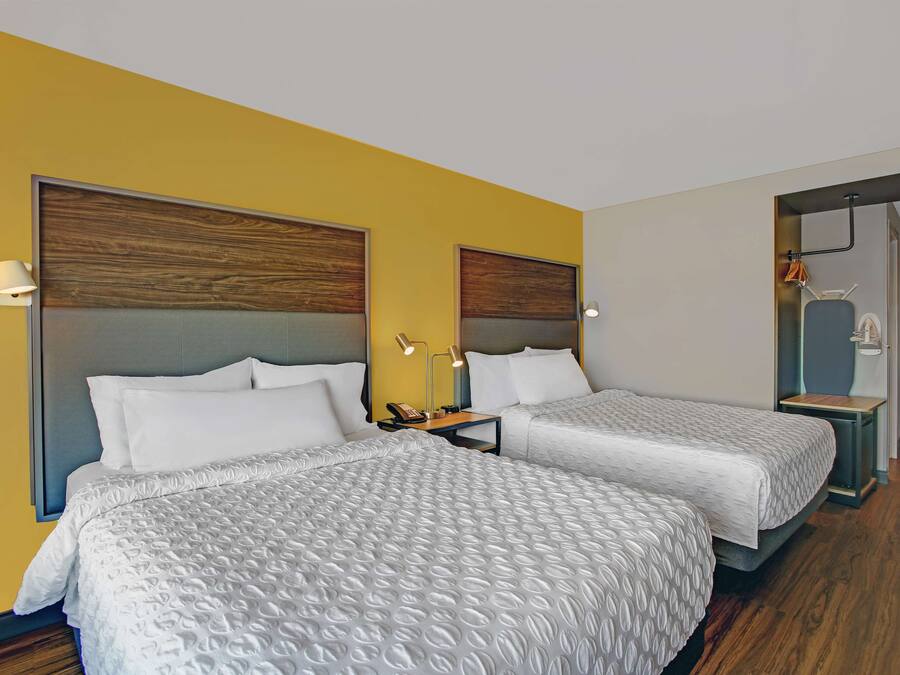 A hotel room with two beds, wooden headboards, a bedside table with a lamp, and a mirror.