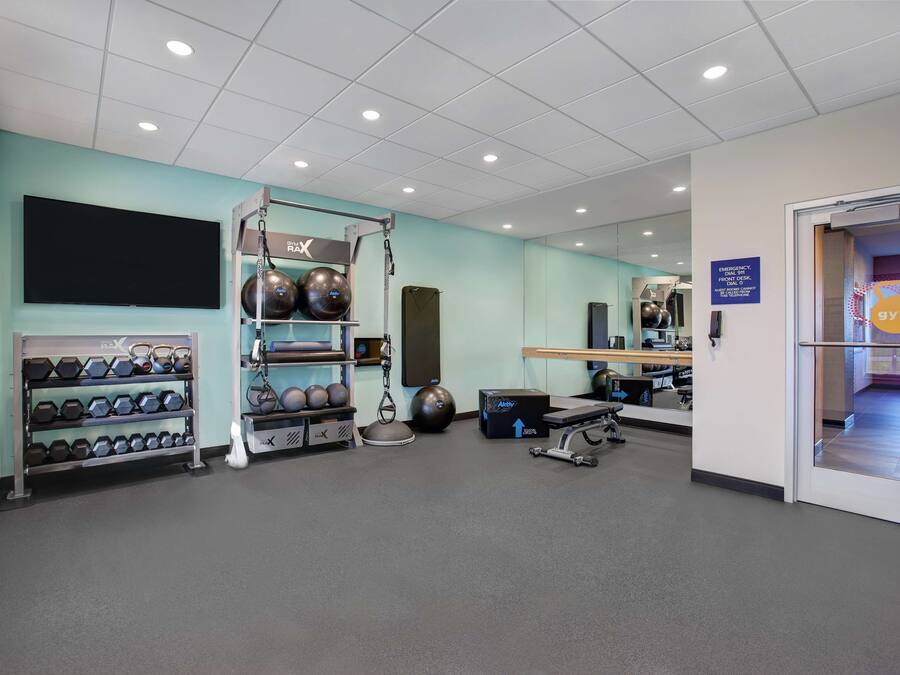 Ein Fitnessraum mit Trainingsgeräten, einem an der Wand befestigten Fernseher und einem Schild, das einen Notfallschalter kennzeichnet.