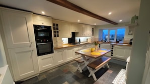 A modern kitchen with white cabinetry, a wooden table, and a view of the outdoors through the windows. - Cosy luxurious 18th century stone built character cottage with stunning views (Penrith)