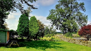 A well-maintained garden with a stone wall, a wooden shed, and a variety of trees. - Cosy luxurious 18th century stone built character cottage with stunning views (Penrith)