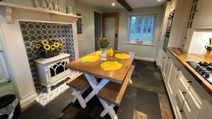 A kitchen with a wooden table, white cabinets, and a decorative wall with the word "COOK". - Cosy luxurious 18th century stone built character cottage with stunning views (Penrith)